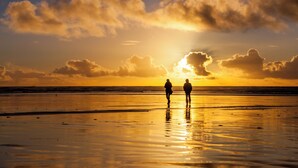 Two people walking on a beach during sunset. - Ebb Tide Oceanfront Inn (Seaside)