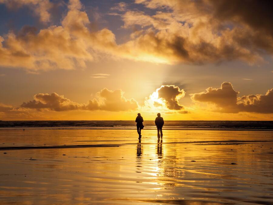 Deux personnes se promènent sur une plage au coucher du soleil.