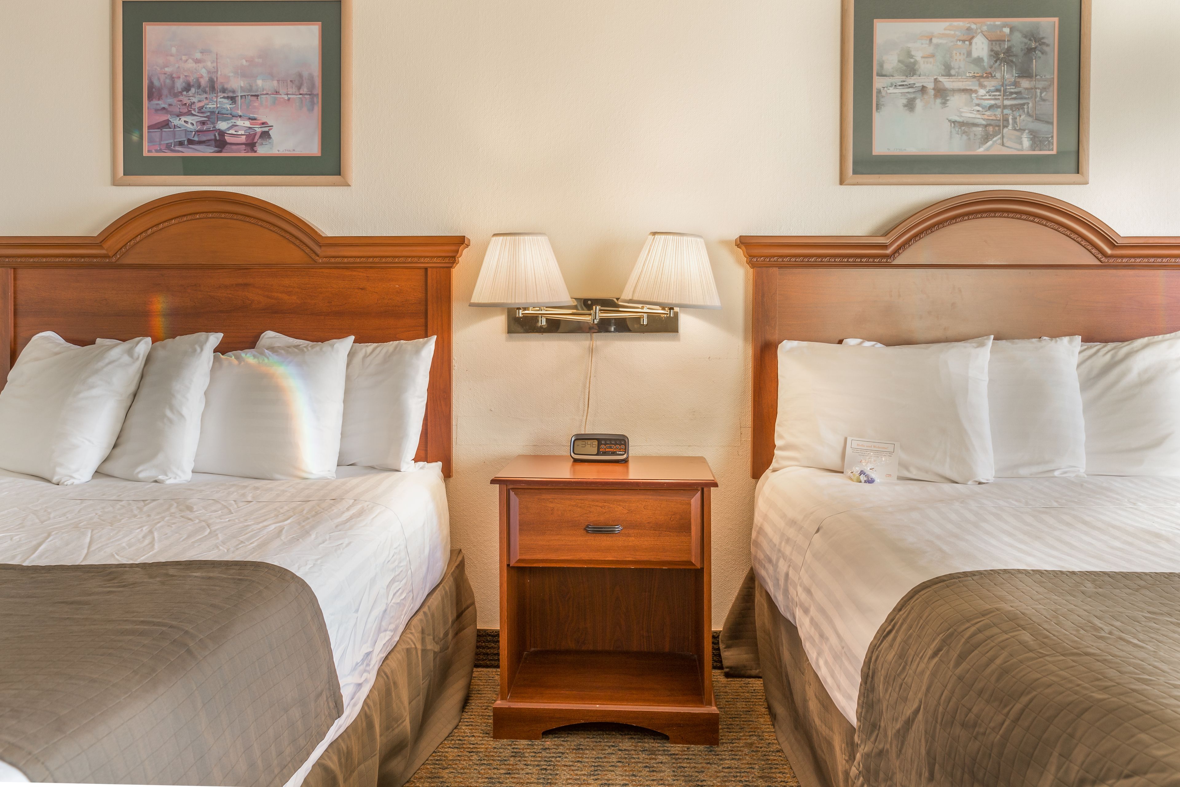 A hotel room with two beds, a nightstand with lamps, and two framed pictures on the wall.