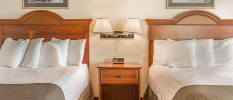 A hotel room with two beds, a nightstand with lamps, and two framed pictures on the wall.