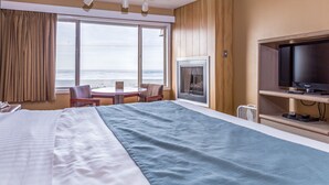 A hotel room with a large bed, a television, a fireplace, and a view of the ocean. - Ebb Tide Oceanfront Inn (Seaside)