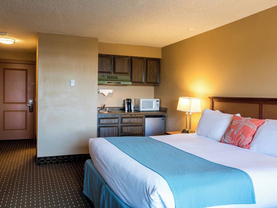 A hotel room with a bed, a desk with a microwave, a coffee maker, and a small kitchenette.