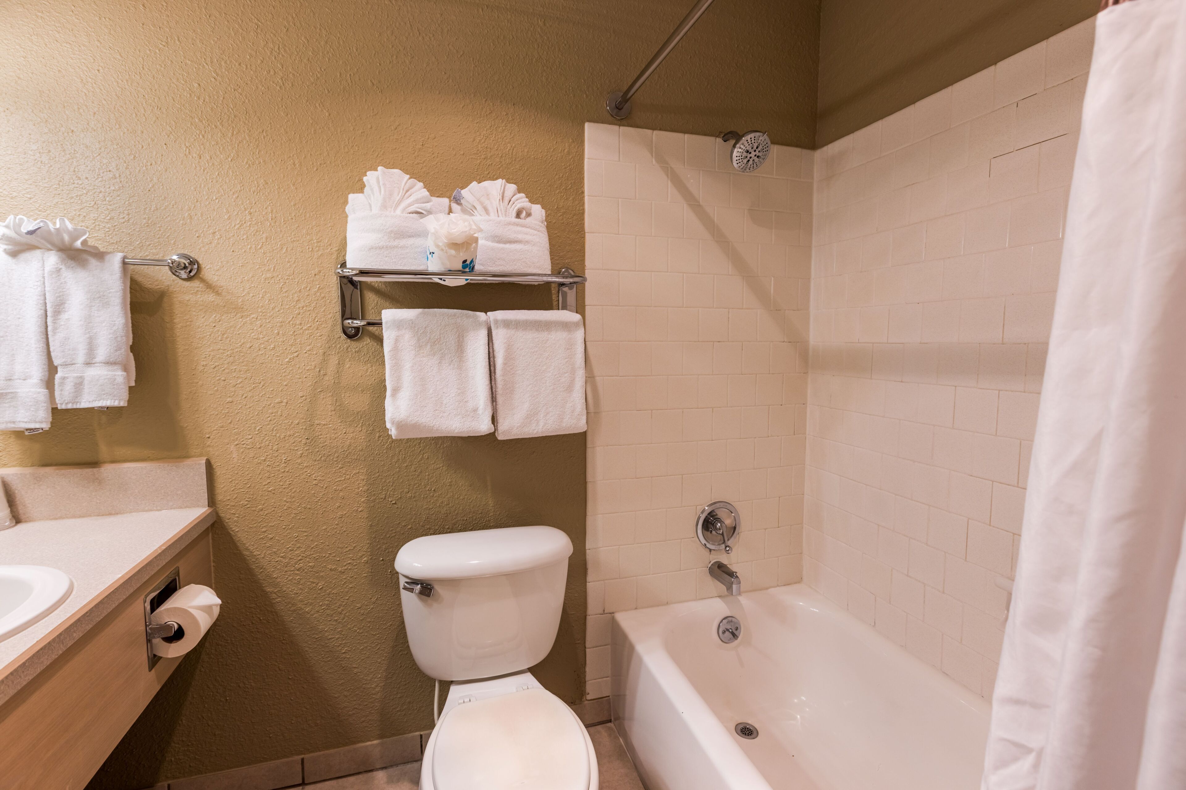 Un baño con inodoro, lavamanos y bañera. Hay toallas en un perchero y una cortina de ducha.