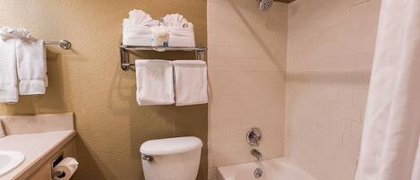 A bathroom with a toilet, sink, and bathtub. There are towels on a rack and a shower curtain.