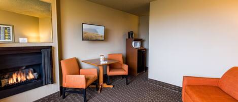 Habitación de hotel con chimenea, una mesa de comedor con dos sillas, un sofá, un microondas y un cuadro en la pared.