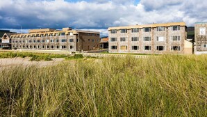 A row of modern multi-story buildings with a flat roof and large windows, situated near a grassy area. - Ebb Tide Oceanfront Inn (Seaside)