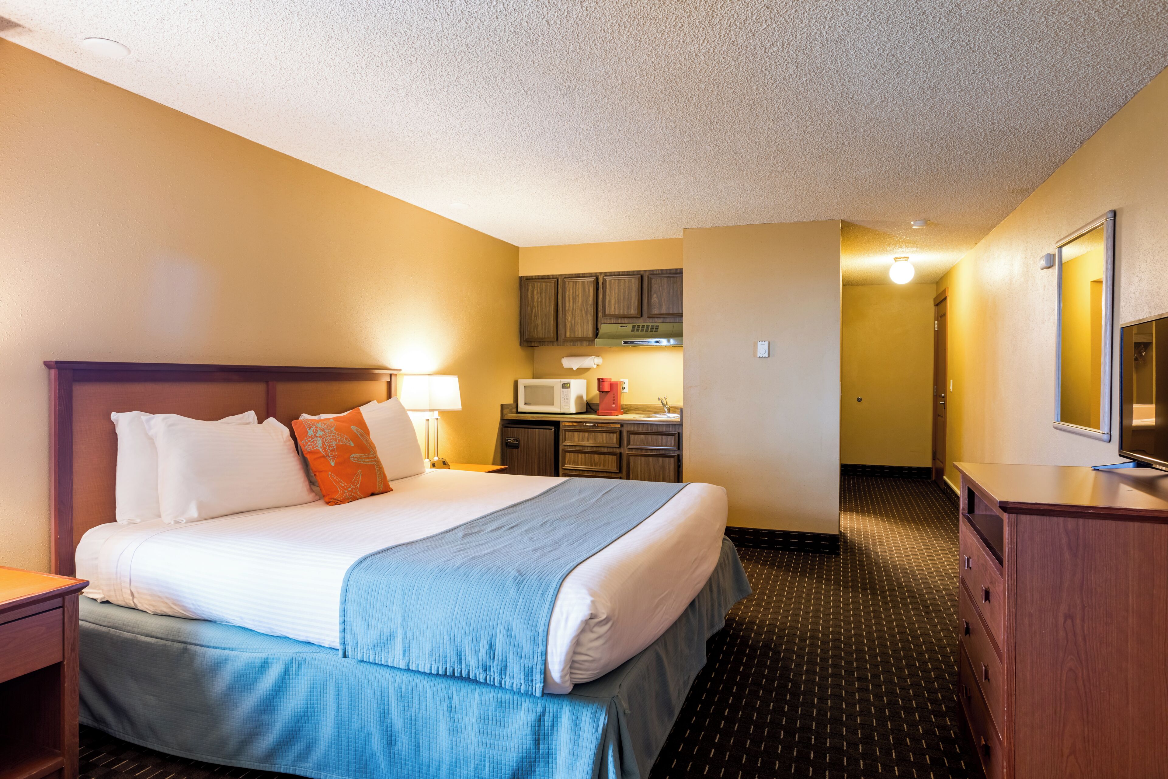 A hotel room with a bed, a desk, a microwave, and a dresser.
