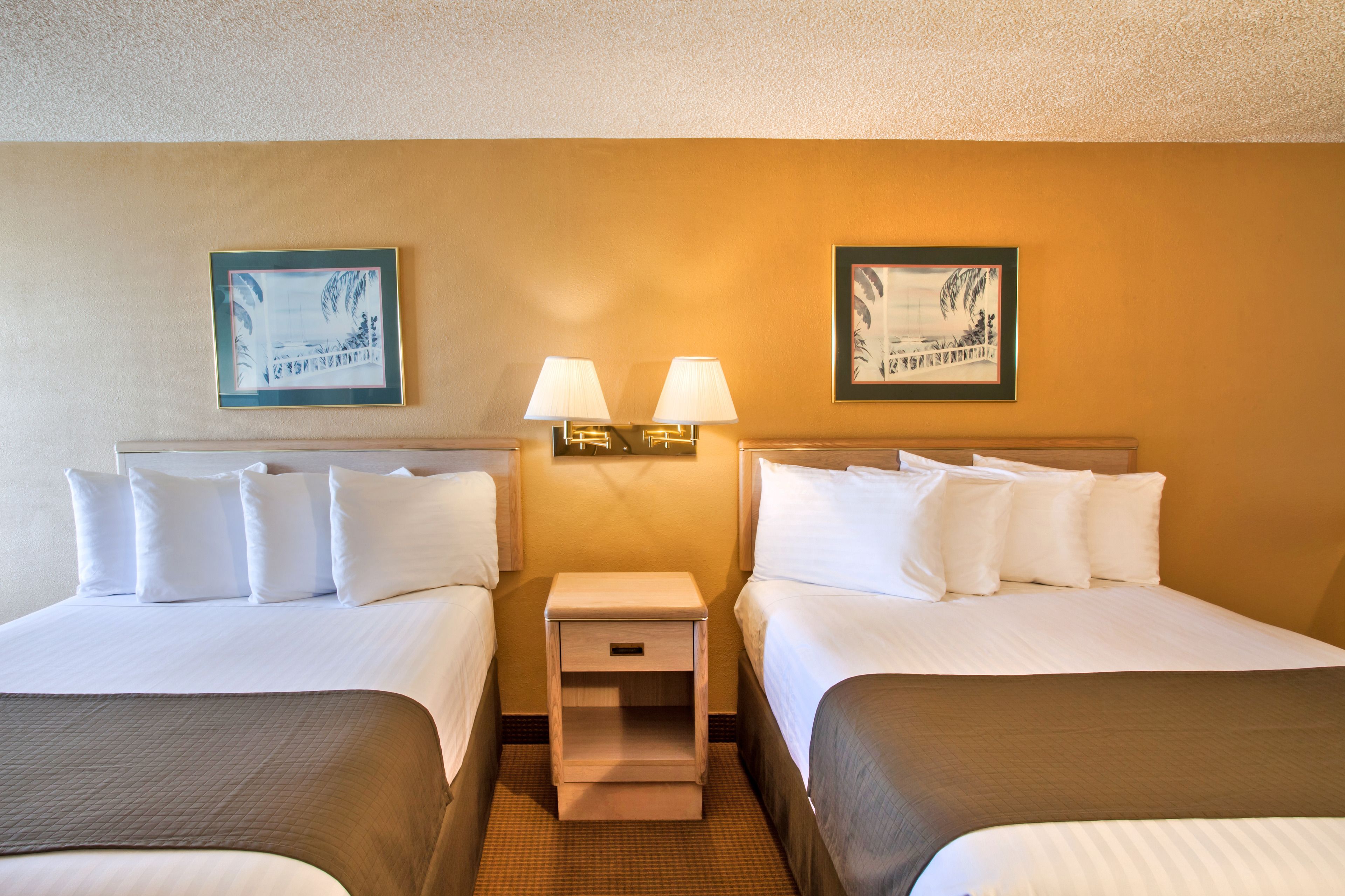 A hotel room with two beds, a nightstand with lamps, and framed artwork on the walls.