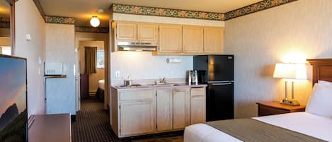 A hotel room with a bed, a desk, a kitchenette, and a TV.