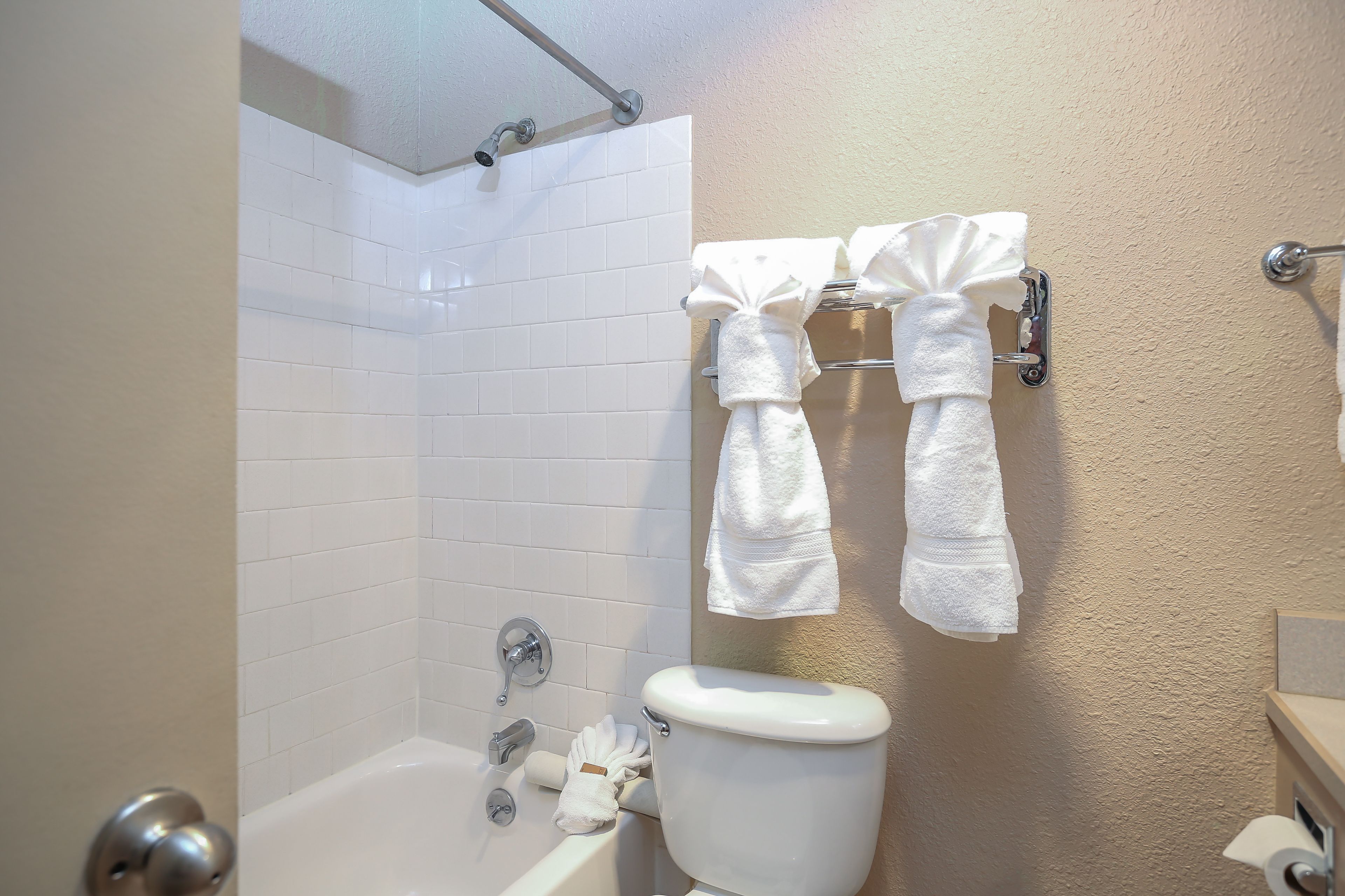 Un baño con paredes de azulejos blancos, una bañera blanca y un inodoro. Hay dos toallas colgadas en un perchero.