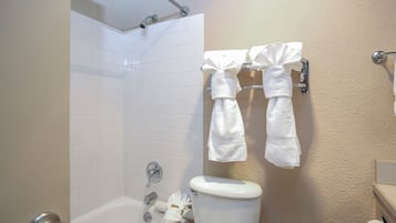 A bathroom with white tiled walls, a white bathtub, and a toilet. There are two towels hanging on a towel rack.