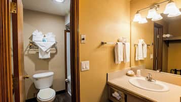 A bathroom with a toilet, sink, and mirror. There are towels and toiletries on the counter.