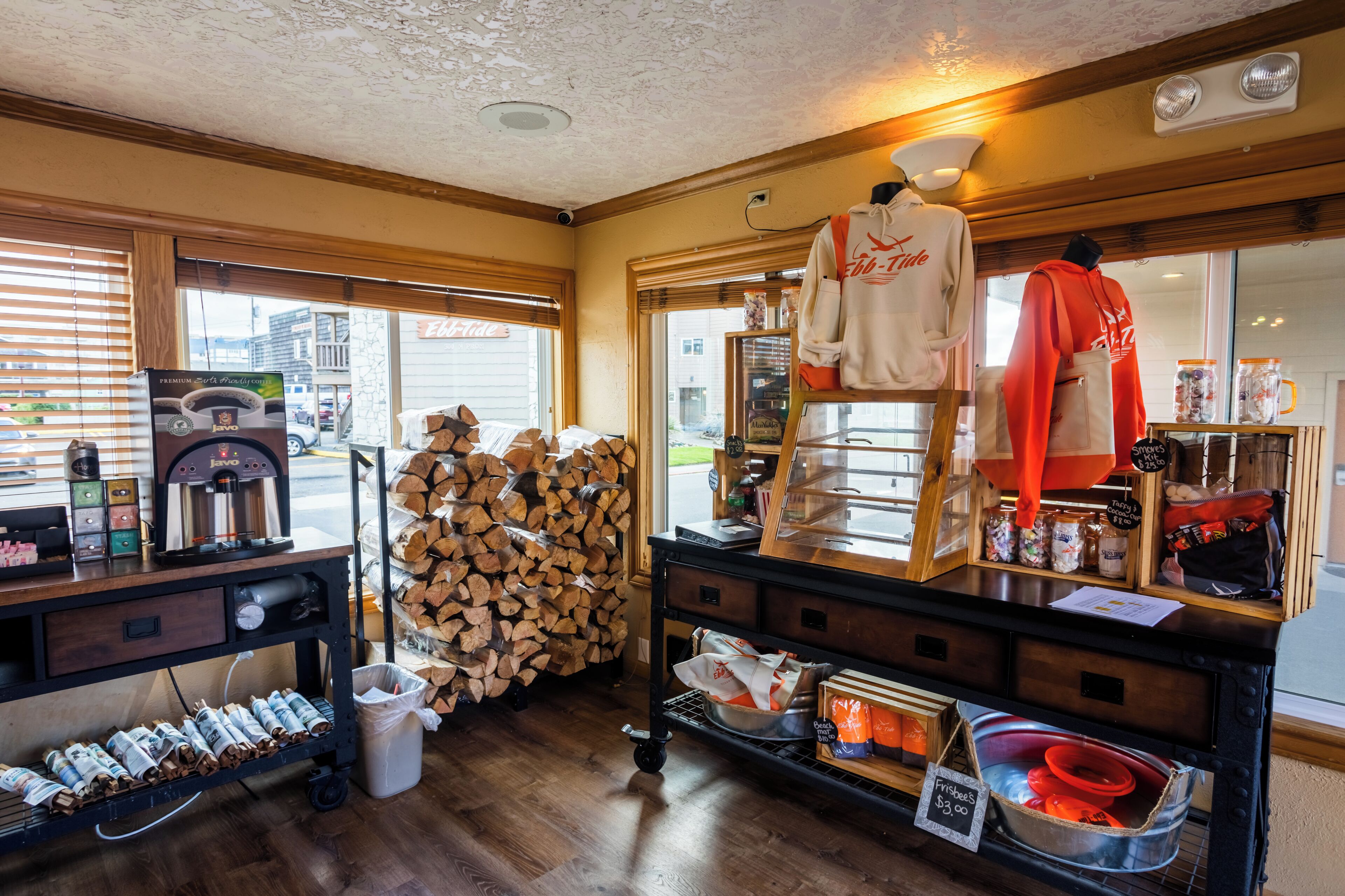 A coffee shop interior with a coffee machine, a stack of firewood, a display of jars, and a mannequin wearing a hoodie.
