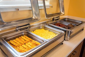 A buffet with various food items including scrambled eggs, bacon, and other meats.