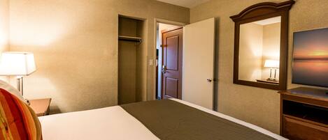 A hotel room with a bed, a dresser, a mirror, a television, and a door leading to another room.