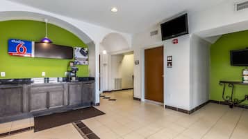 A hotel lobby with a reception desk, a sign for 'Studio 6 Extended Stay', a television mounted on the wall, and a door marked 'Guest Services'.