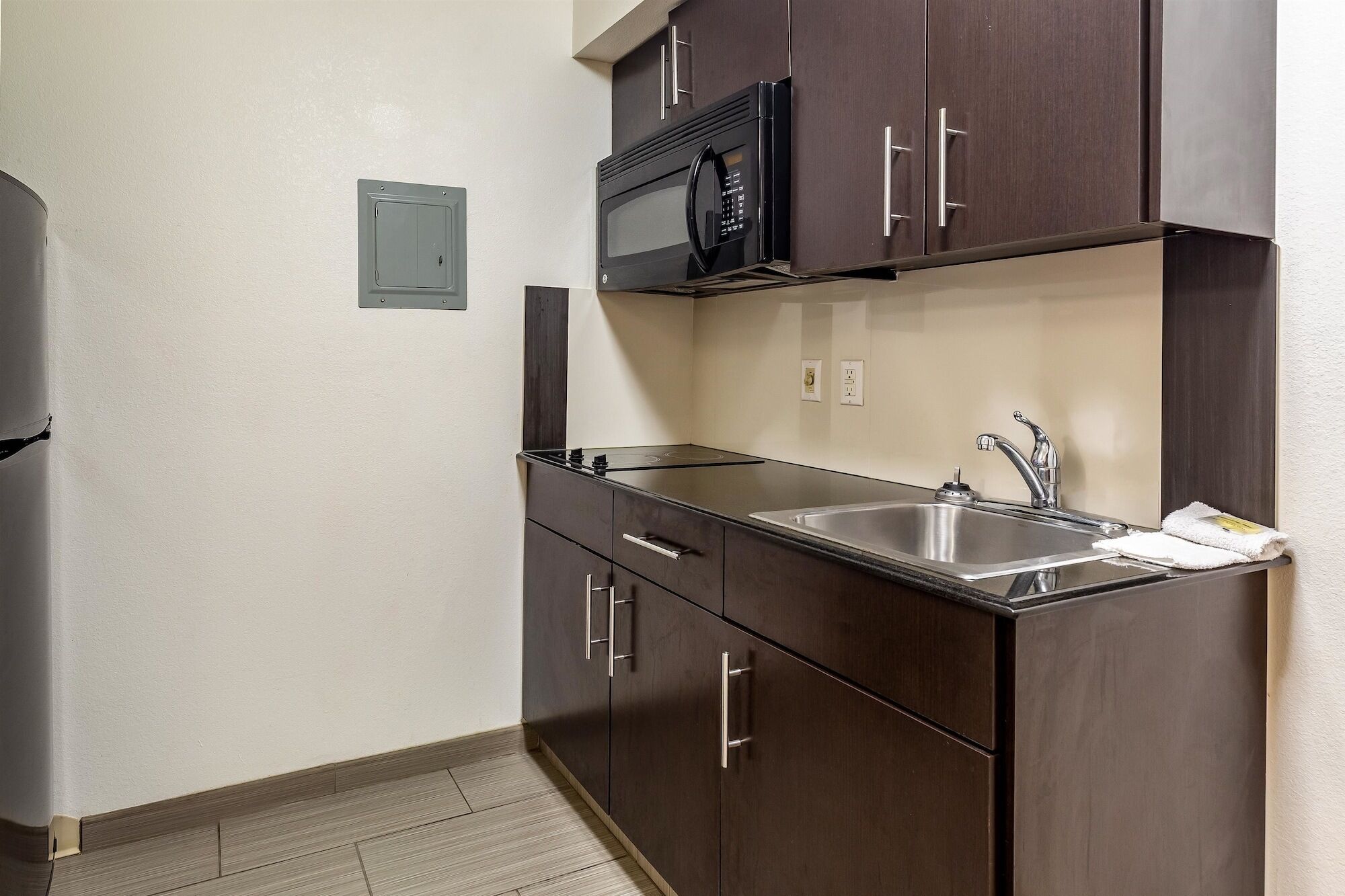 A compact kitchen with dark cabinets, a stainless steel sink, and a microwave.