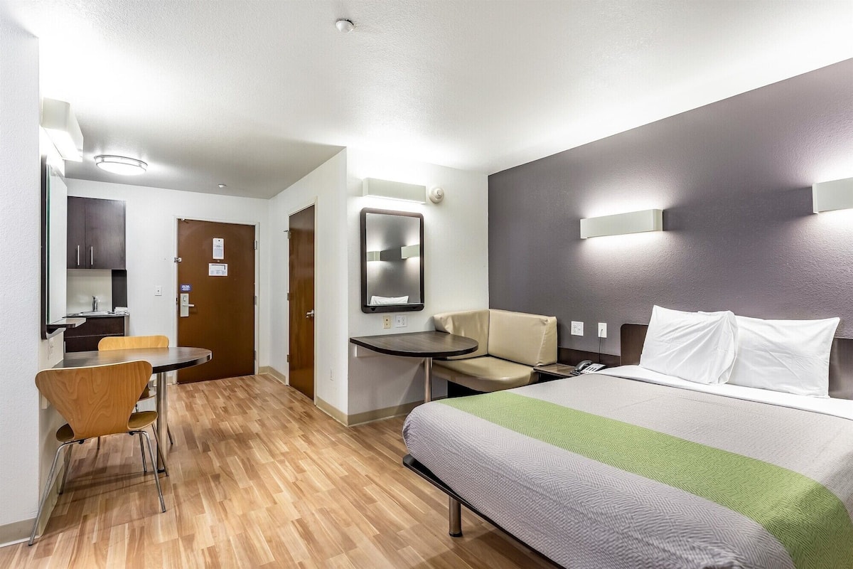 Ett hotellrum med en säng, ett skrivbord, en stol, ett litet bord och en spegel.