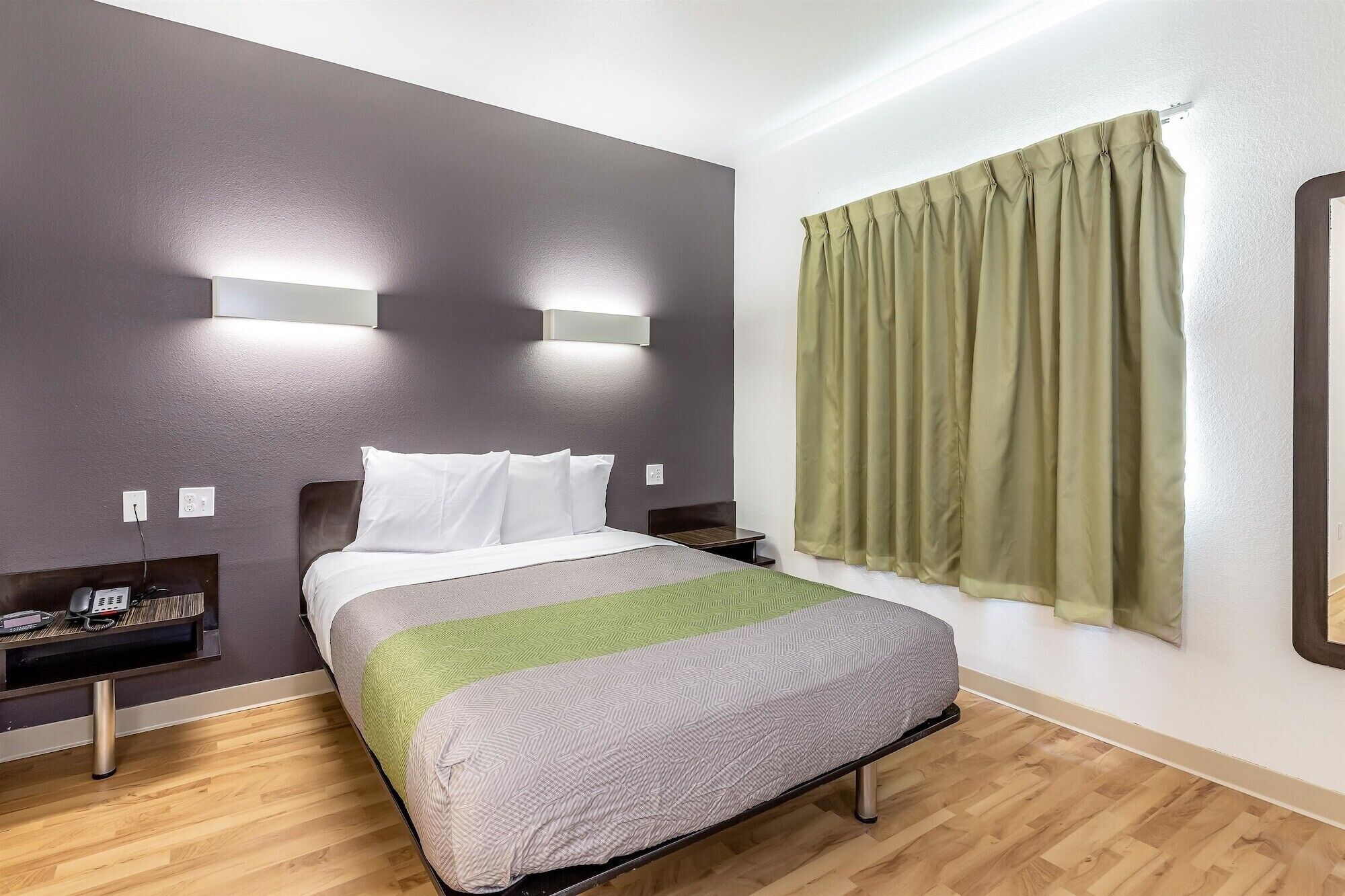 Una habitación de hotel con cama, mesitas de noche, teléfono y ventana con cortinas.
