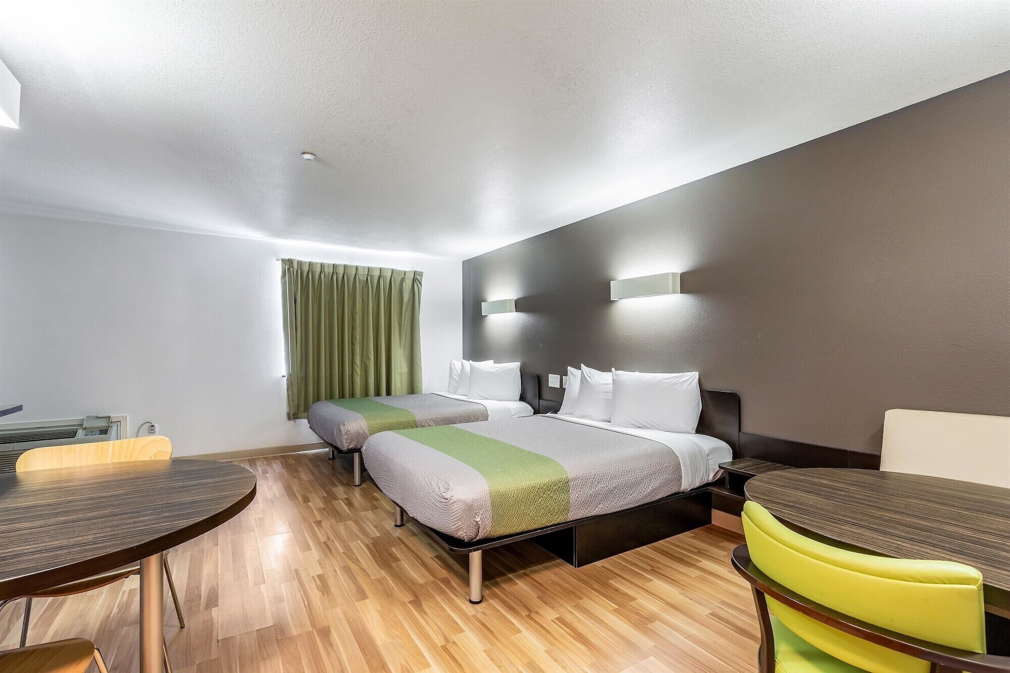 A hotel room with two beds, a dining table, and a yellow chair.