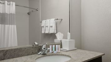 A bathroom with a granite countertop sink, a mirror, a towel rack with white towels, and a tissue box.