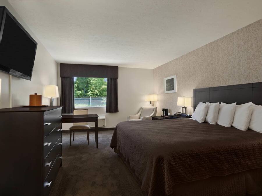 A hotel room with a large bed, a desk, a chair, a television, and a window with curtains.