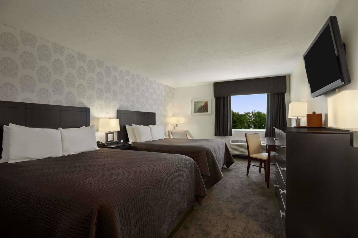 A hotel room with two beds, a desk, a TV, and a window with a view.