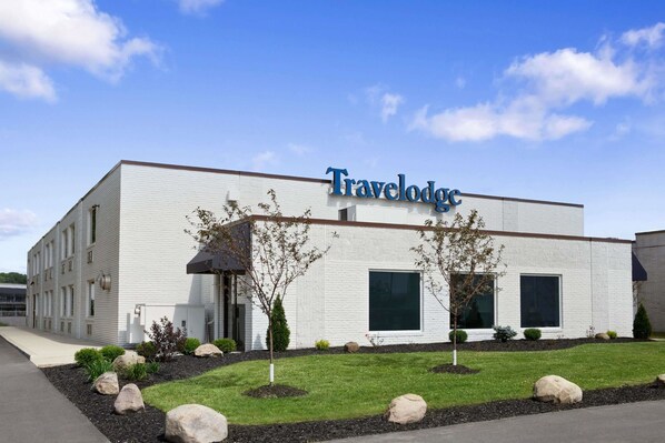 A Travelodge hotel with a white exterior, large windows, and a landscaped front yard with rocks and shrubs.