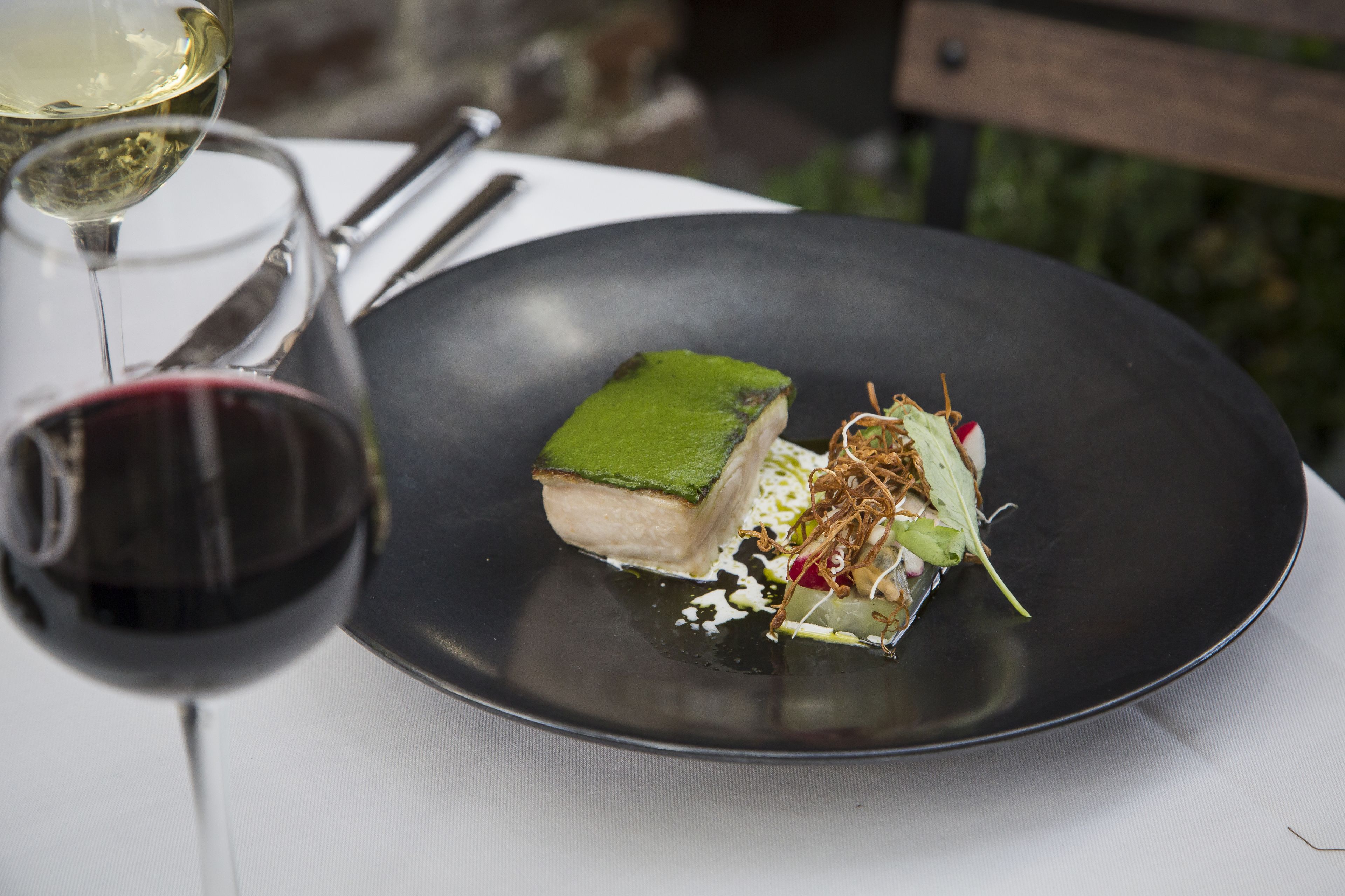 Un plato negro con un guiso, una copa de vino tinto y otra de vino blanco.