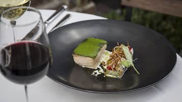 Un plato negro con un guiso, una copa de vino tinto y otra de vino blanco.