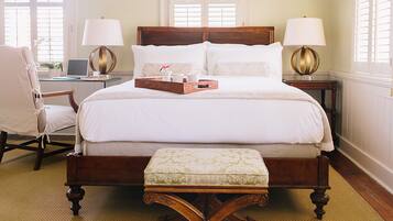 A large bed with a wooden frame, two bedside tables with lamps, a chair, and a small table with a tray of items.