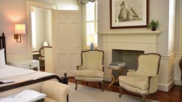A hotel room with a bed, two armchairs, a small table, a fireplace, and a framed picture on the wall.
