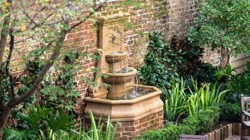 Un mur de briques agrémenté d’une fontaine en pierre, un banc en bois et une table en verre, le tout dans un cadre de jardin.
