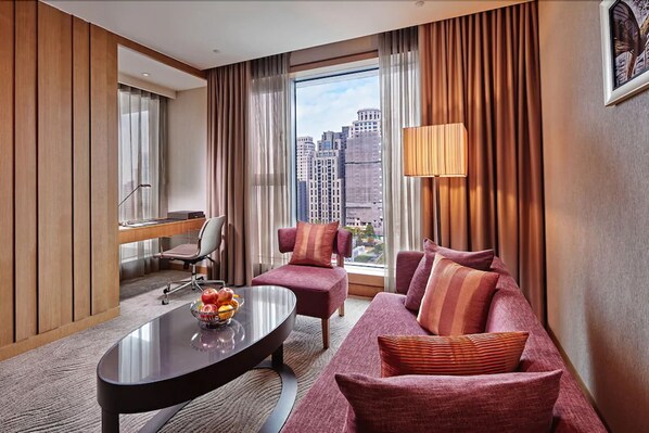 Une chambre d’hôtel avec une grande fenêtre, un canapé, un fauteuil, une table basse et une lampe.