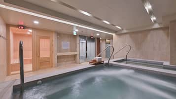 A modern indoor pool with a wooden sauna area, a digital clock, and a sign indicating the sauna's temperature.