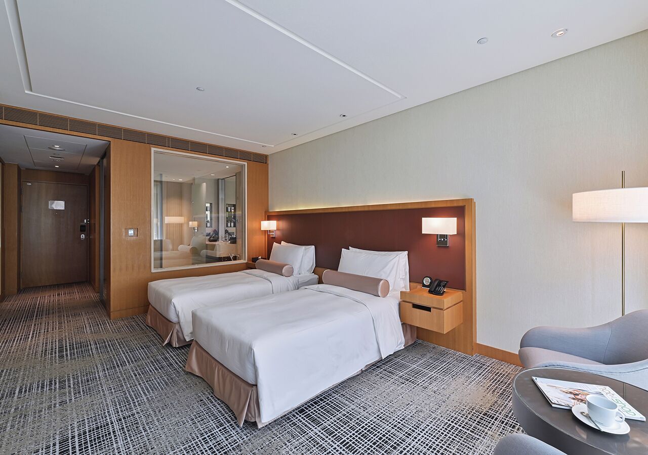 A hotel room with two beds, a sitting area, a desk, and a mirror.
