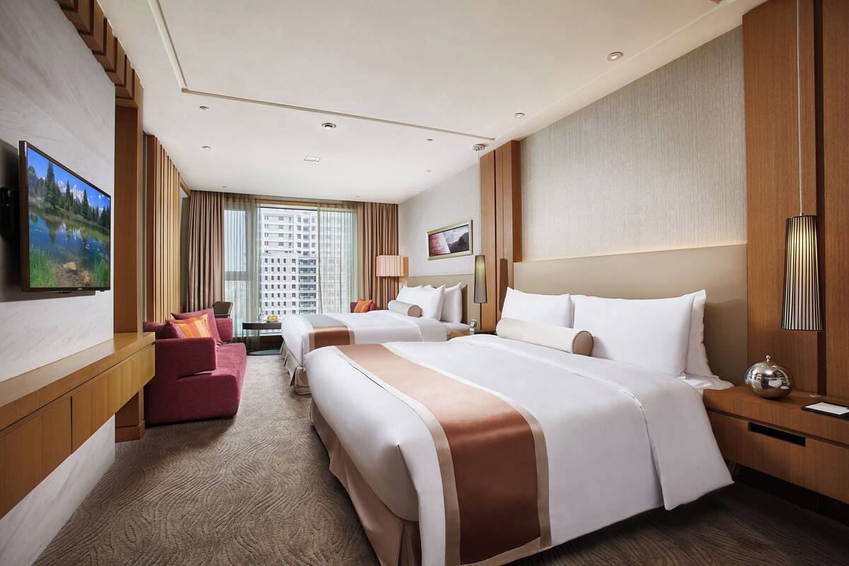 Habitación de hotel con dos camas, televisión, escritorio y vista a un paisaje urbano.