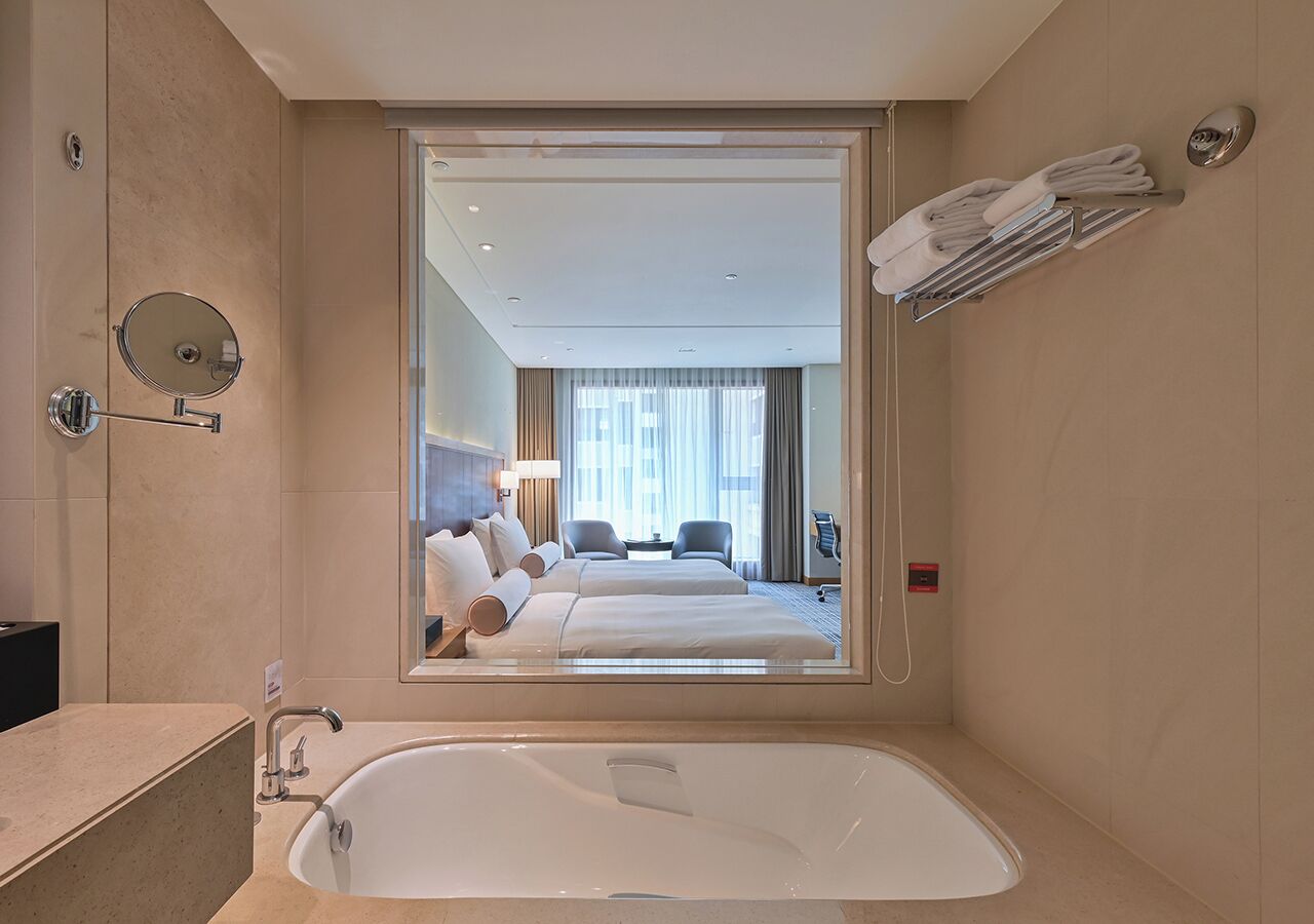 A hotel room with a large mirror reflecting a bed and a bathroom.