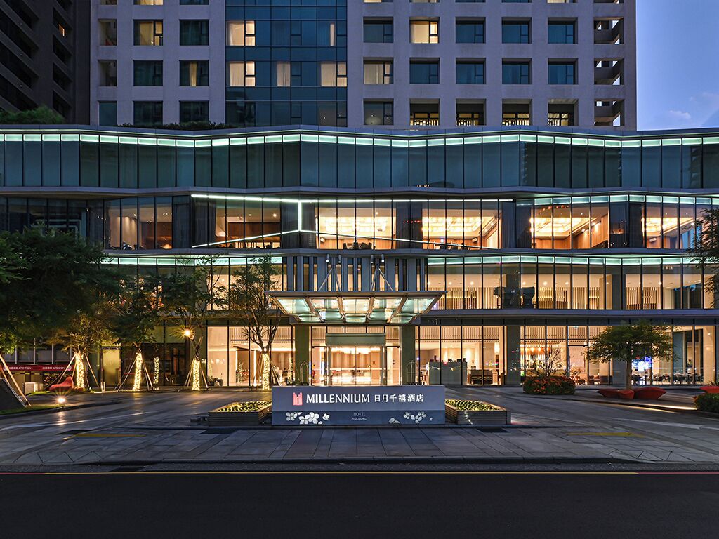 A multi-story hotel with a modern glass facade, a prominent entrance, and a sign indicating it is a hotel.