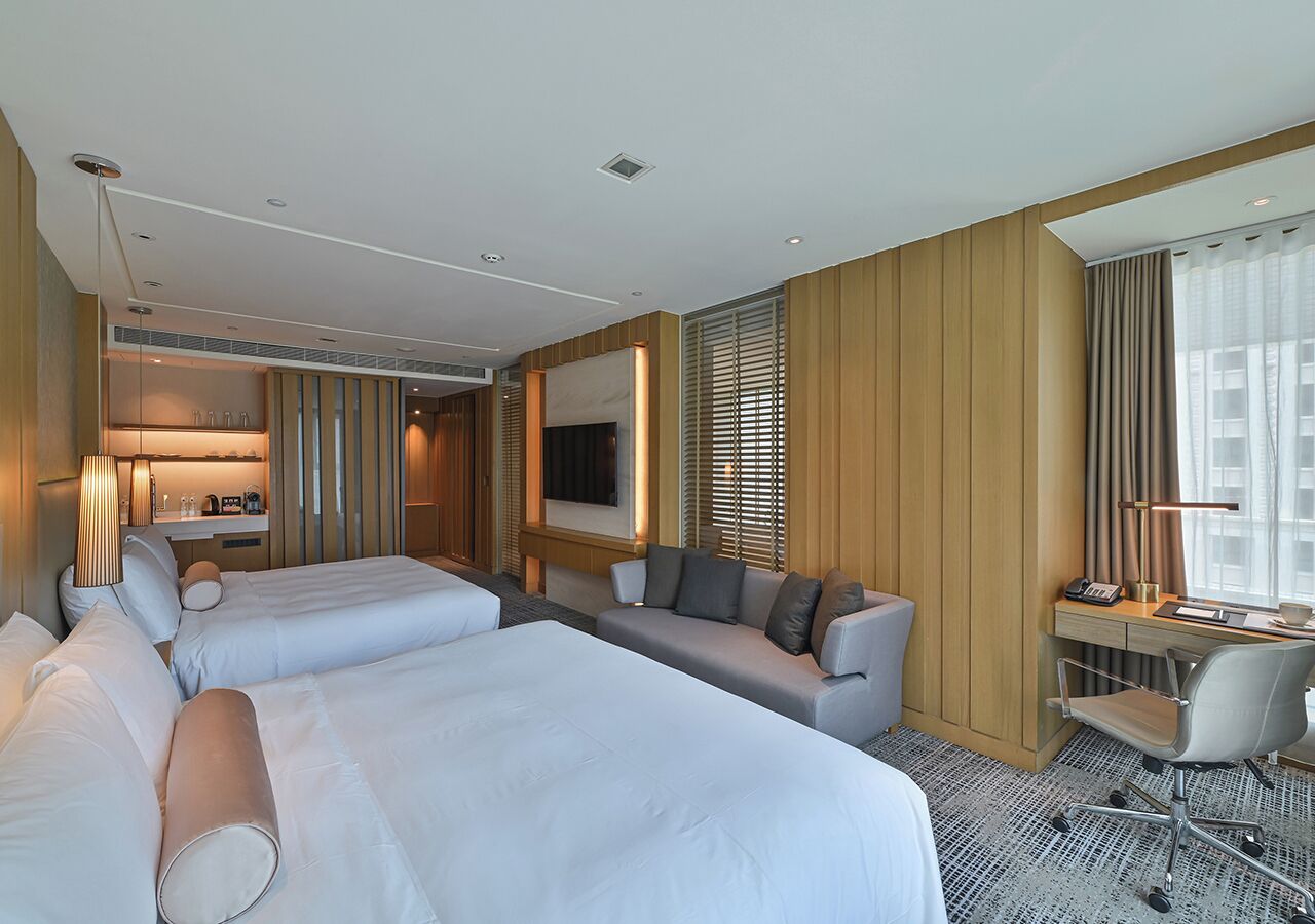 A hotel room with two beds, a sofa, a desk, and a television.