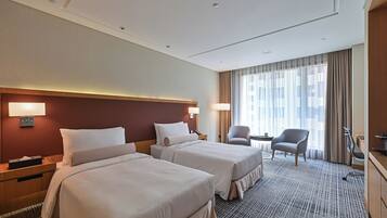 A hotel room with two beds, a desk, a chair, and a large window with curtains.