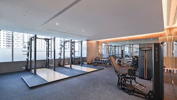 A modern gym with weightlifting equipment, a mirror wall, and a view of buildings outside.