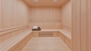 Una sauna de madera con bancos, un banco con toallas y una rejilla de ventilación.