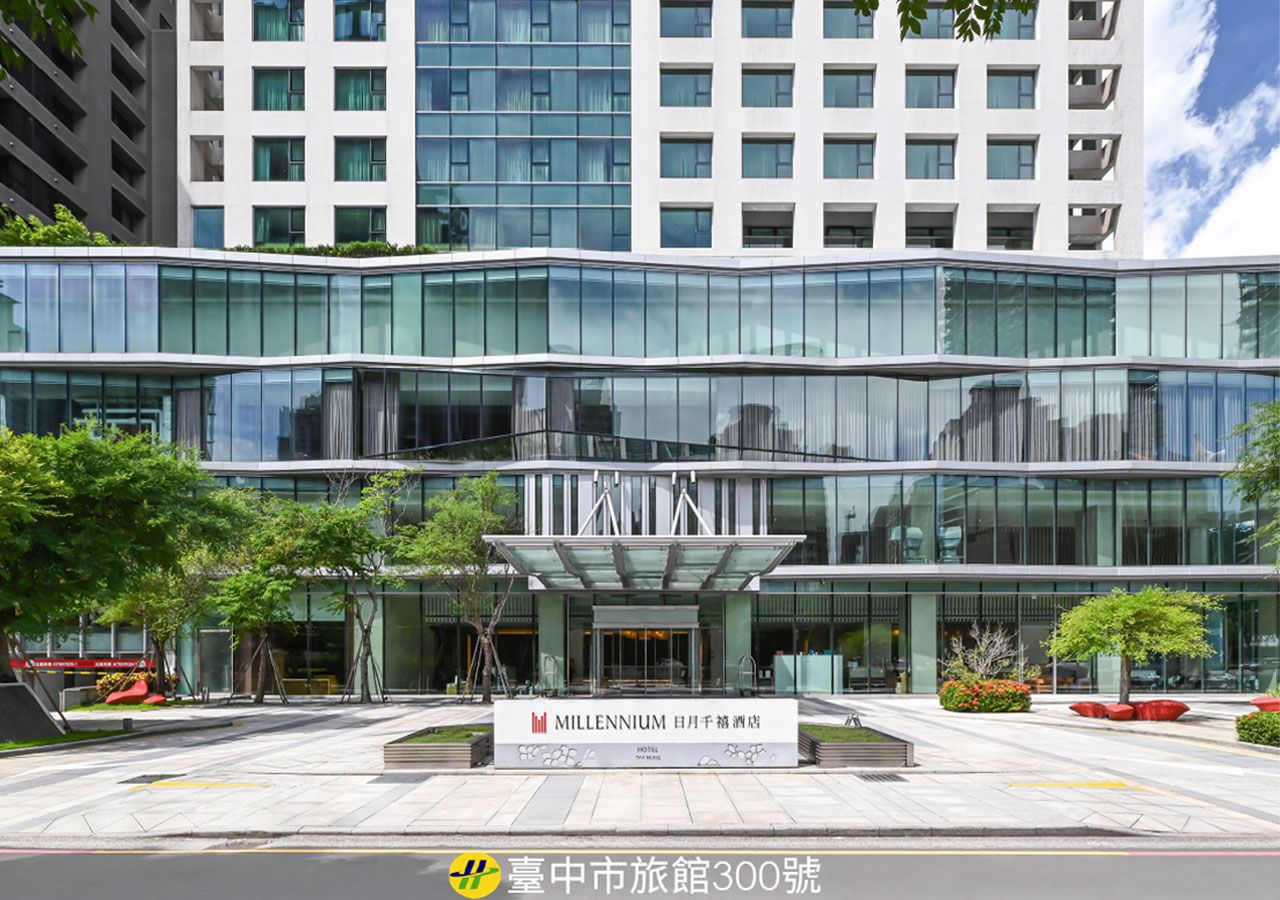 A modern hotel with a glass facade, a prominent entrance, and a sign indicating it is the Millennium Hotel.