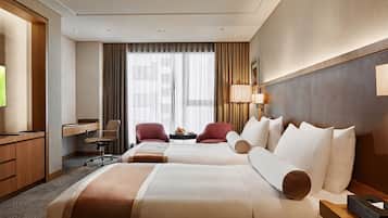 A hotel room with two beds, a desk, a chair, a TV, and a window with curtains.