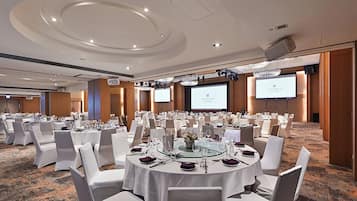 Une salle de conférence avec des tables rondes, des chaises blanches et un sol recouvert de moquette.