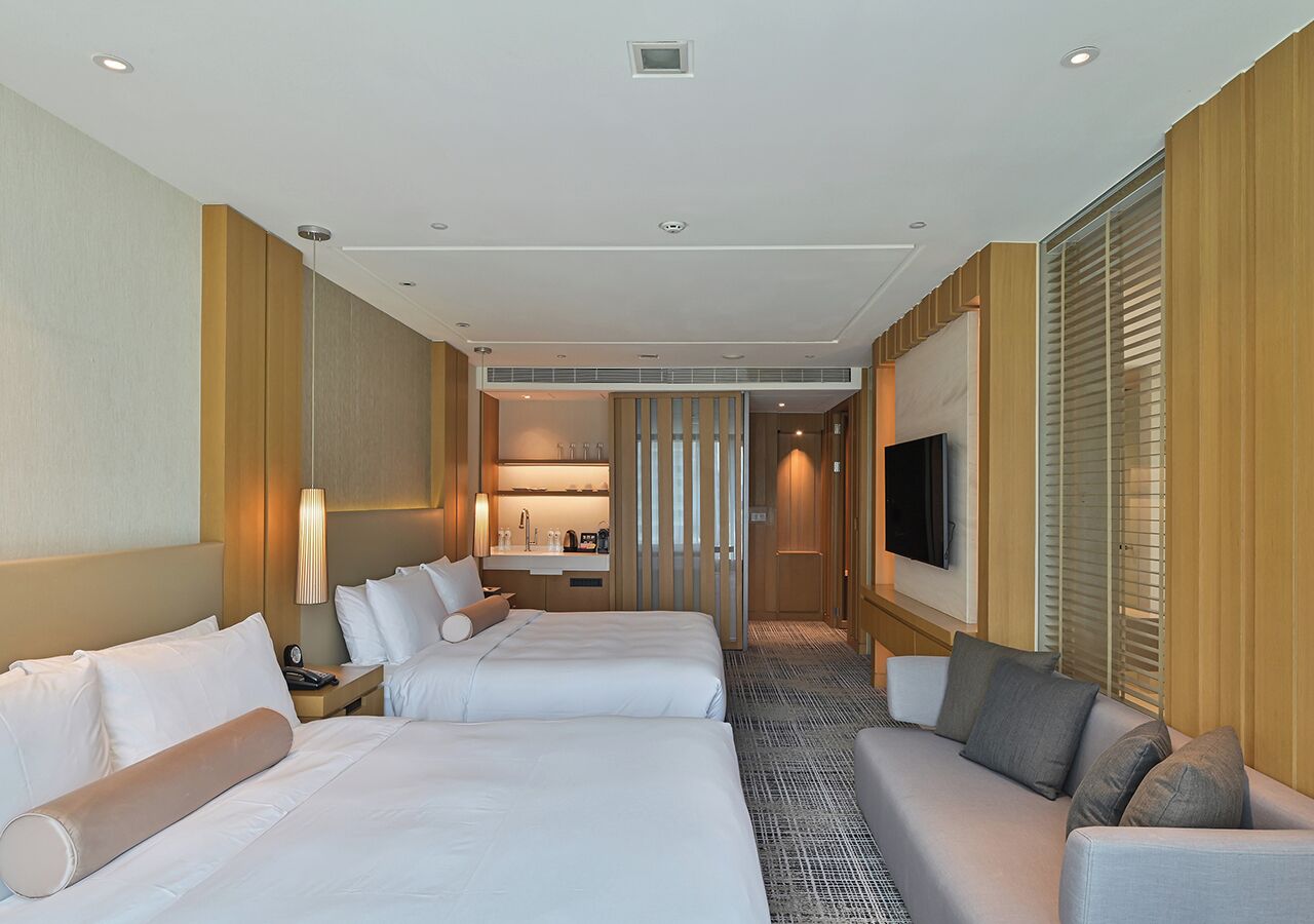 Quarto de hotel com duas camas, um sofá, uma televisão e uma cozinha compacta.