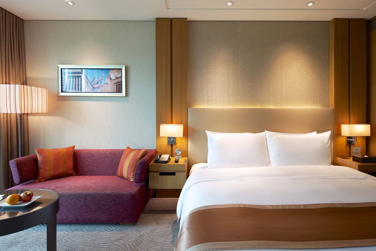 Un cuarto de hotel con una cama grande, un sofá, una mesita de noche con lámpara, un cuadro en la pared y un teléfono.