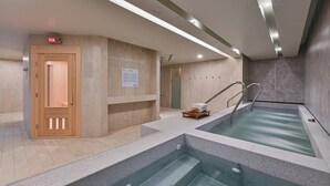 Una piscina interior moderna con agua cristalina, bancos de madera y una zona de sauna.