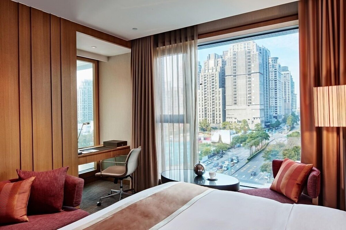 Una habitación de hotel con una cama grande, un escritorio, una silla y vistas a edificios altos.